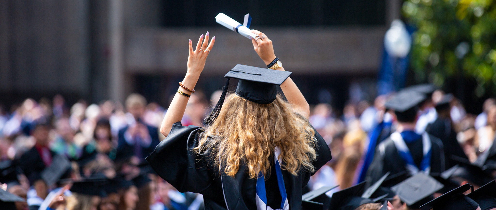 A graduating woman stands with her back to the camera.
