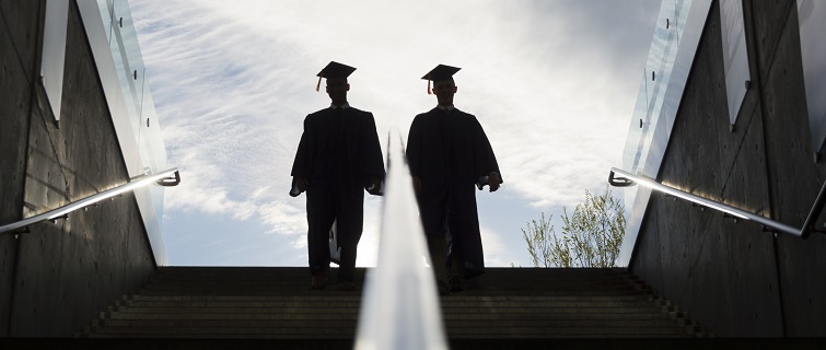 Two graduates in full regalia walking down stairs