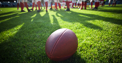 Football resting on field with team in the background