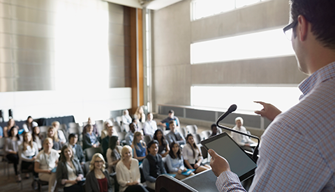 Businessman speaks in front of crowded auditorium