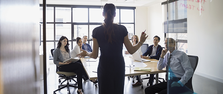 Woman addressing a board room with a diverse attendees