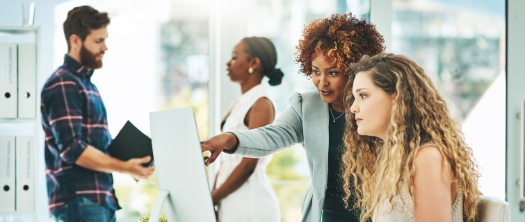 Two businesswomen working together on a computer in an office.